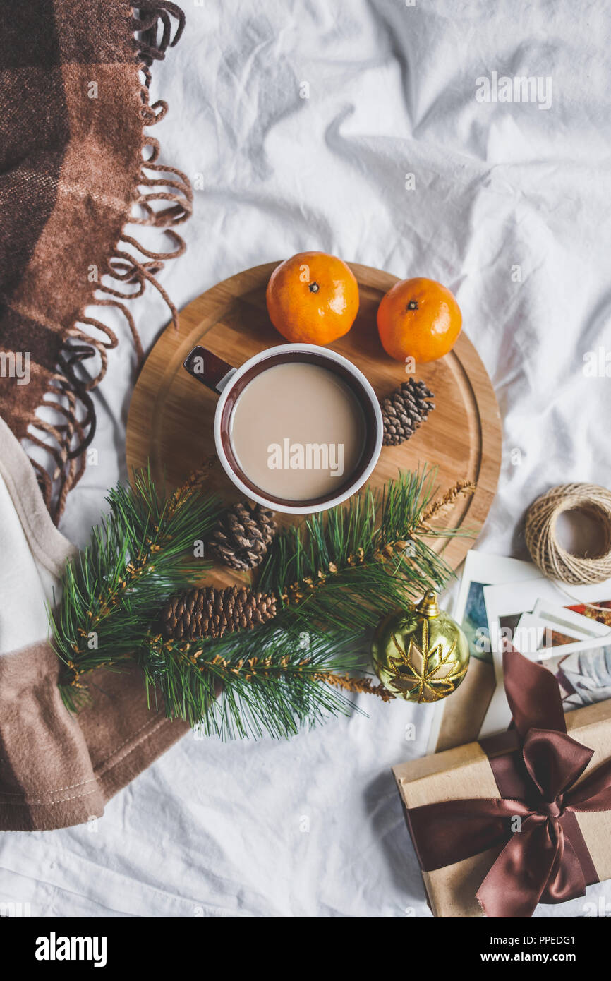 Winter gemütliche Konzept. Tasse mit Kaffee auf einem Tablett, Mandarinen, Cookies, tanne Zweig, plaid auf dem Bett Weihnachtskarte mockup Stockfoto