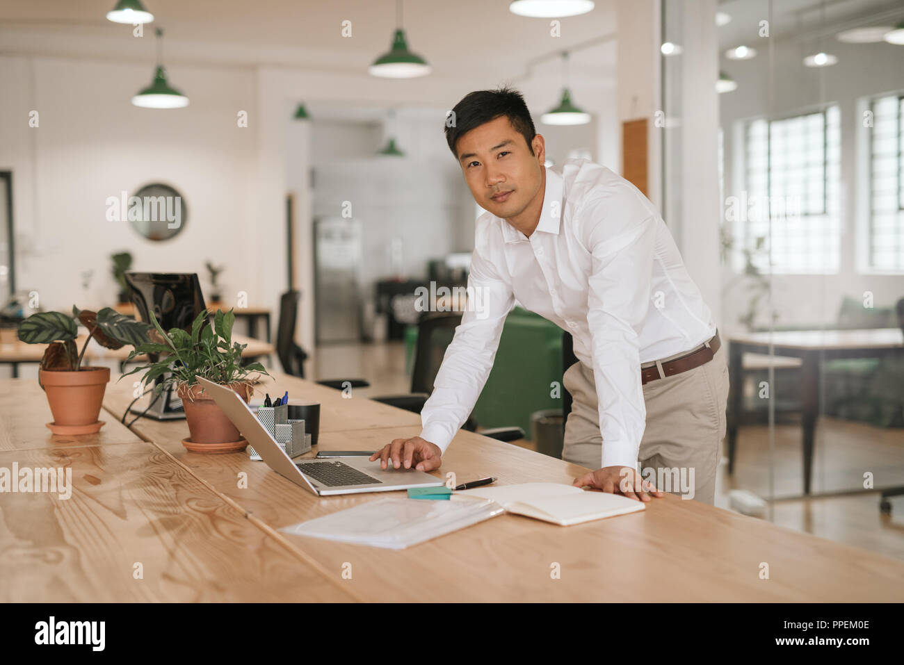 Junge asiatische Geschäftsmann lehnte sich auf seinem Schreibtisch mit einem Laptop Stockfoto