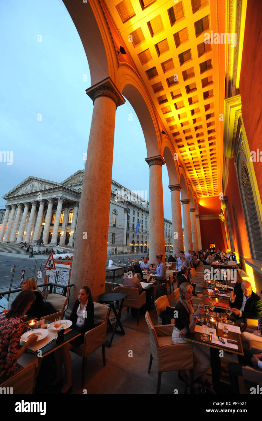 Gäste können auf der Terrasse des Restaurants "kufflers California Kitchen" in das Gebäude der ehemaligen Residenzpost auf den Max-Joseph-Platz in München. Im Hintergrund, der Bayerischen Staatsoper. Stockfoto