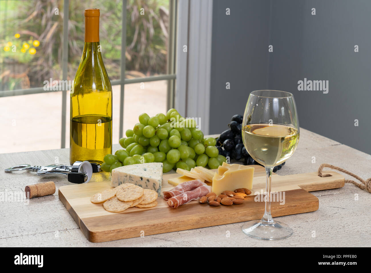 Glas Weißwein mit Flasche Wein, Käse, Cracker, Schinken, Mandeln und Trauben Stockfoto