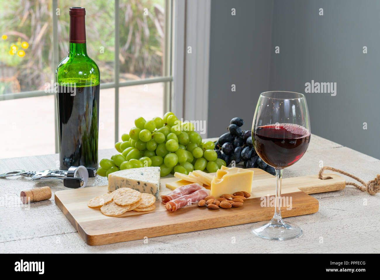 Glas Rotwein mit Flasche Wein, Käse, Cracker, Schinken, Mandeln und Trauben Stockfoto