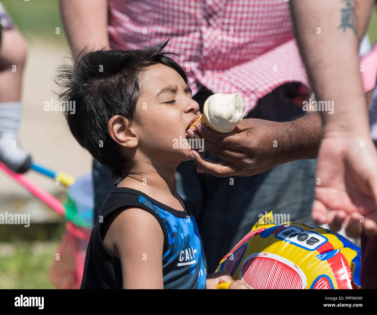 Jungen asiatischen Kind ein Eis im Sommer in England, Großbritannien gefüttert zu werden. Stockfoto