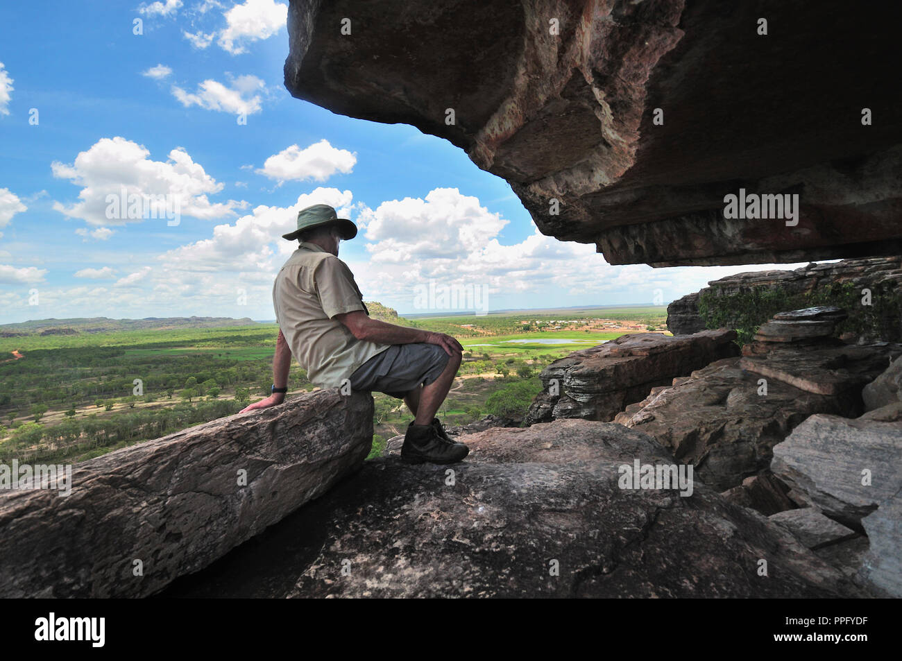 Ein männlicher Tourist, der unter einer Felskunstgalerie auf dem Injalak Hill sitzt und die herrliche Aussicht auf Arnhem Land, Northern Territory, Australien, betrachtet Stockfoto