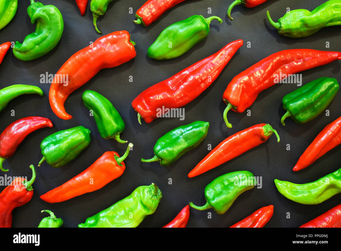 Rote und grüne Paprika formen Muster auf einem dunklen Hintergrund. Gemüse und Lebensmittel abstrakt Hintergrund. Ansicht von oben. Bio Lebensmittel und Formen. Stockfoto
