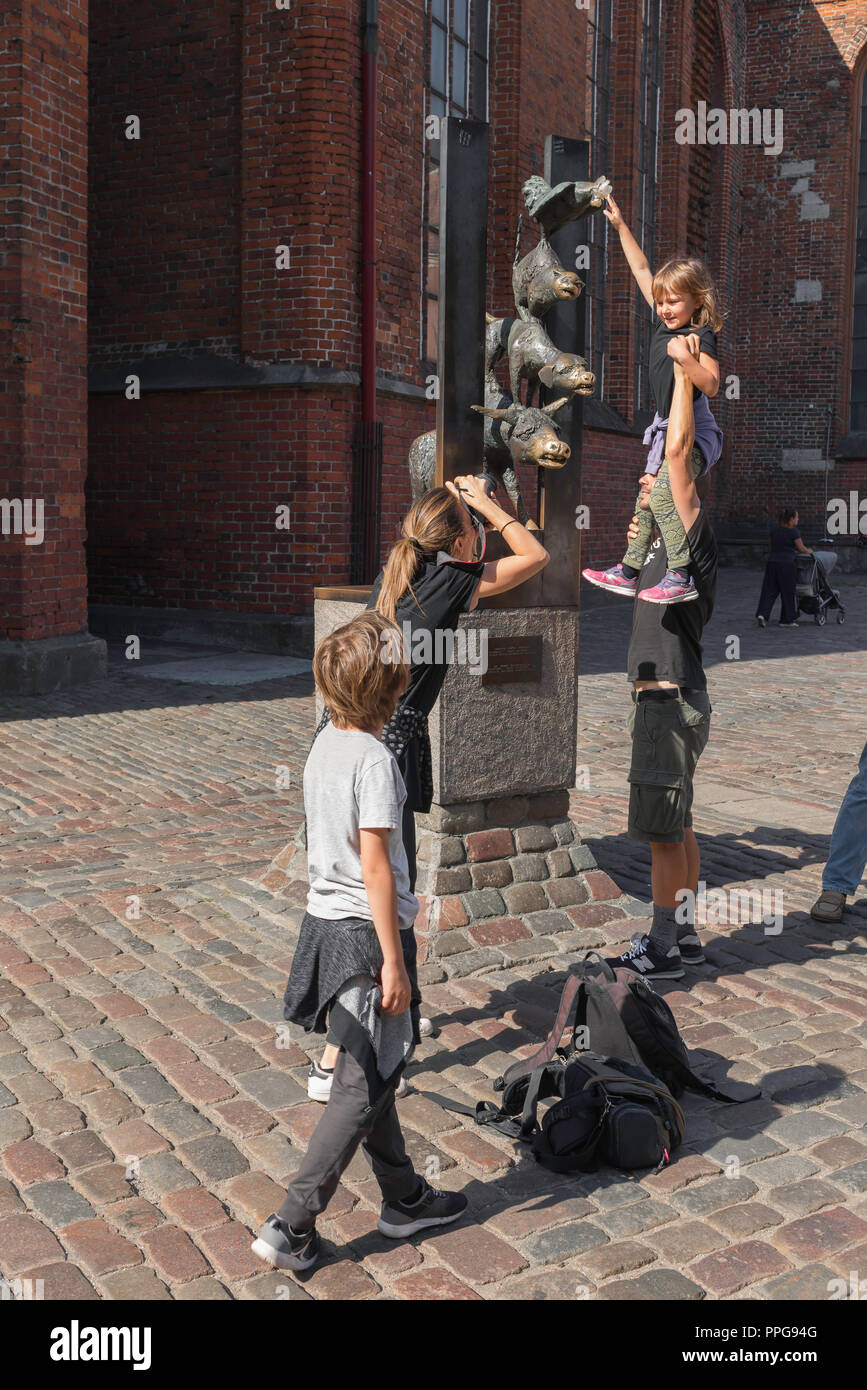 Ein Vater und eine Tochter posieren für ein Foto während der berühmten Bremer Stadtmusikanten Skulptur im mittelalterlichen Zentrum der Altstadt von Riga, Lettland besuchen. Stockfoto