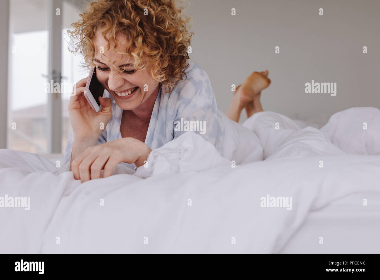 Glückliche Frau Gespräch am Handy im Bett nach dem Aufwachen am Morgen. Frau Gespräch am Handy, während sie sich auf dem Bett. Stockfoto
