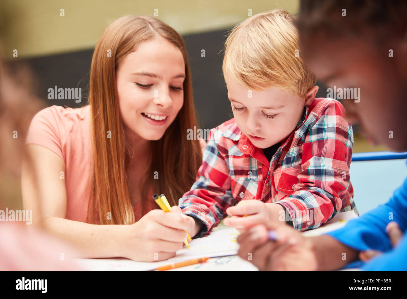 Frau als Erzieher oder Erzieherin hilft Kindern in den Malkurs der Kindertagesstätte zu zeichnen Stockfoto