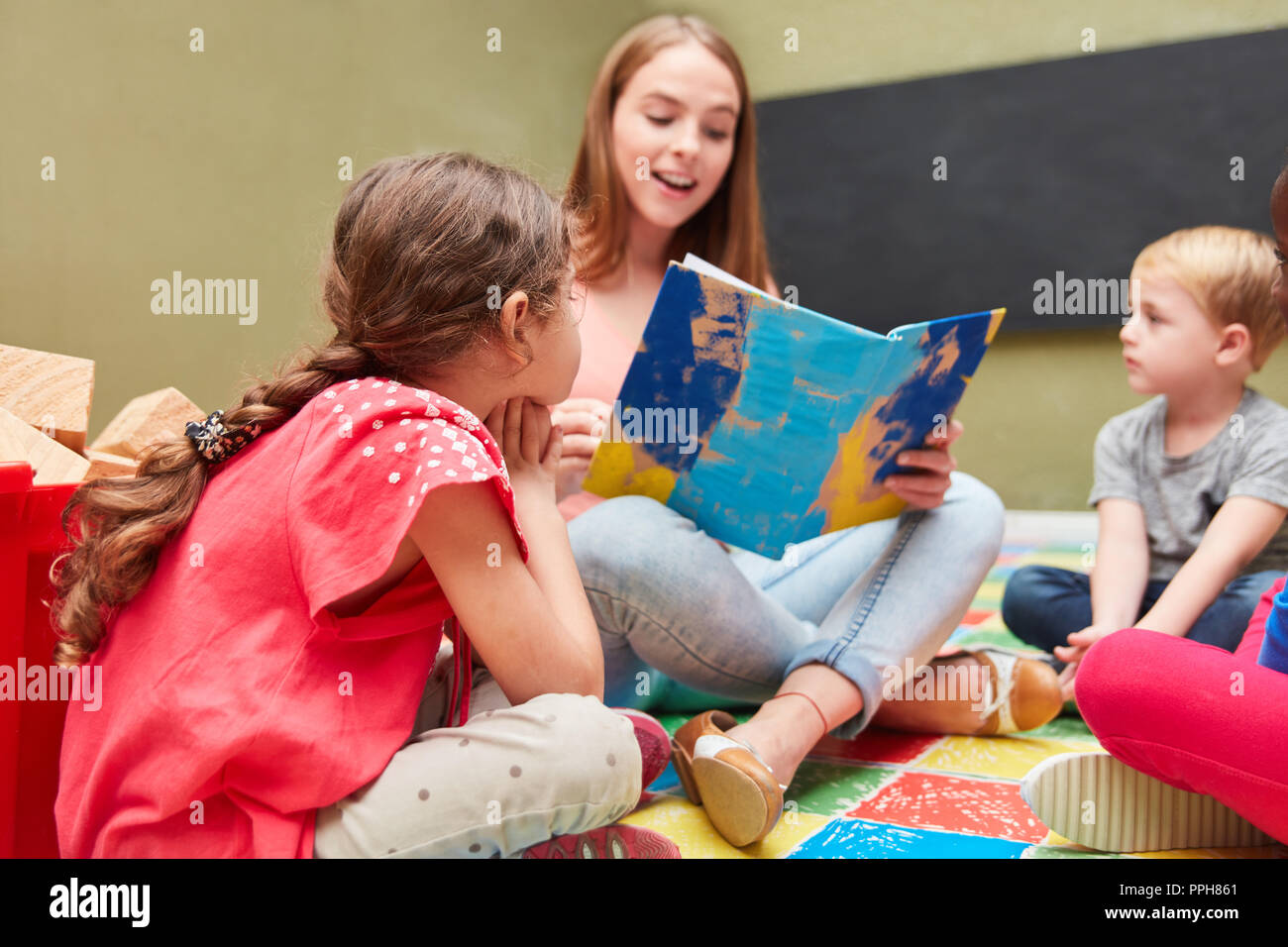 Tagesmutter und Kinder lesen aus einem Kinderbuch in einem Kindergarten Stockfoto