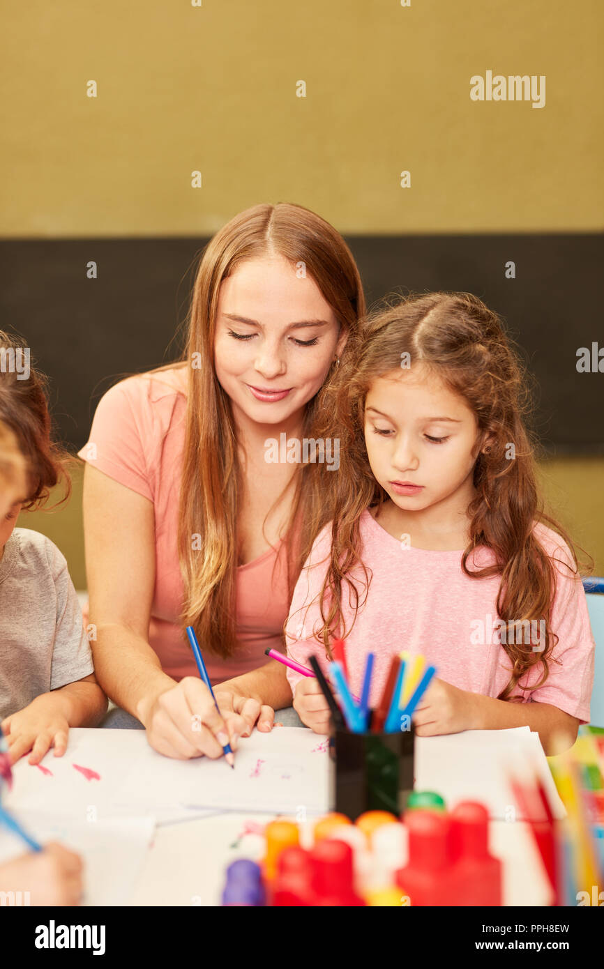 Frau als Erzieherin hilft ein Mädchen beim Zeichnen in der Malerei Klasse im Kindergarten Stockfoto