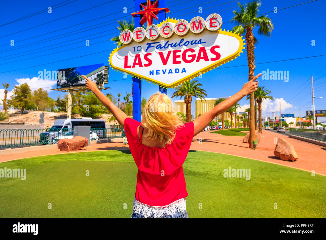 Sorglos Frau mit erhobenen Armen an Willkommen im fabelhaften Las Vegas Nevada Schild, beliebte Sehenswürdigkeit auf dem Las Vegas Strip am Eingang der Stadt. Happy Tourist in Nevada, USA. Blue Sky. Stockfoto