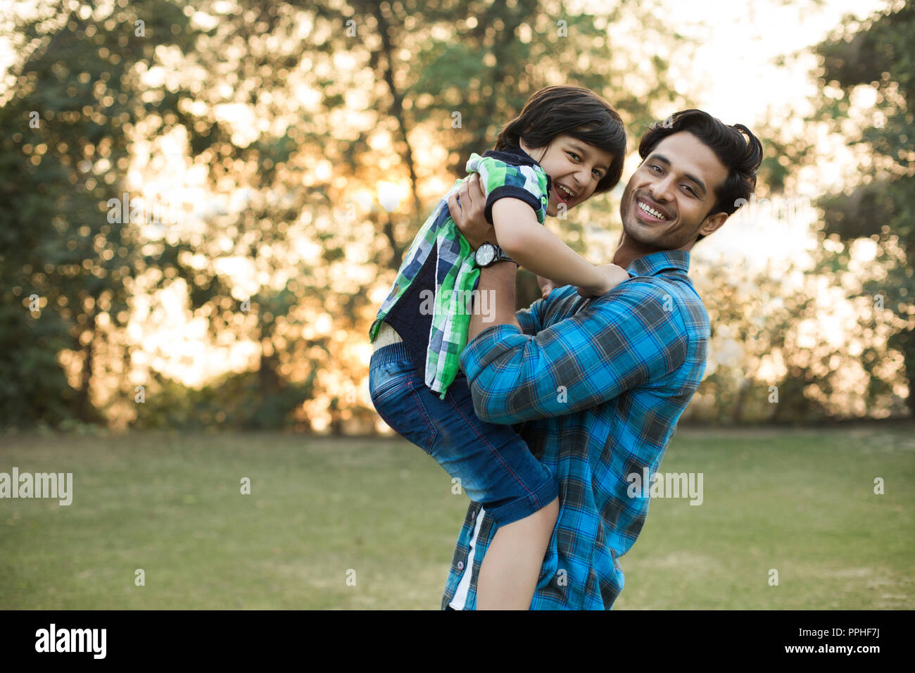 Lächelnd Mann spielt mit seinem glücklichen Sohn von ihm Heben in den Park. Stockfoto