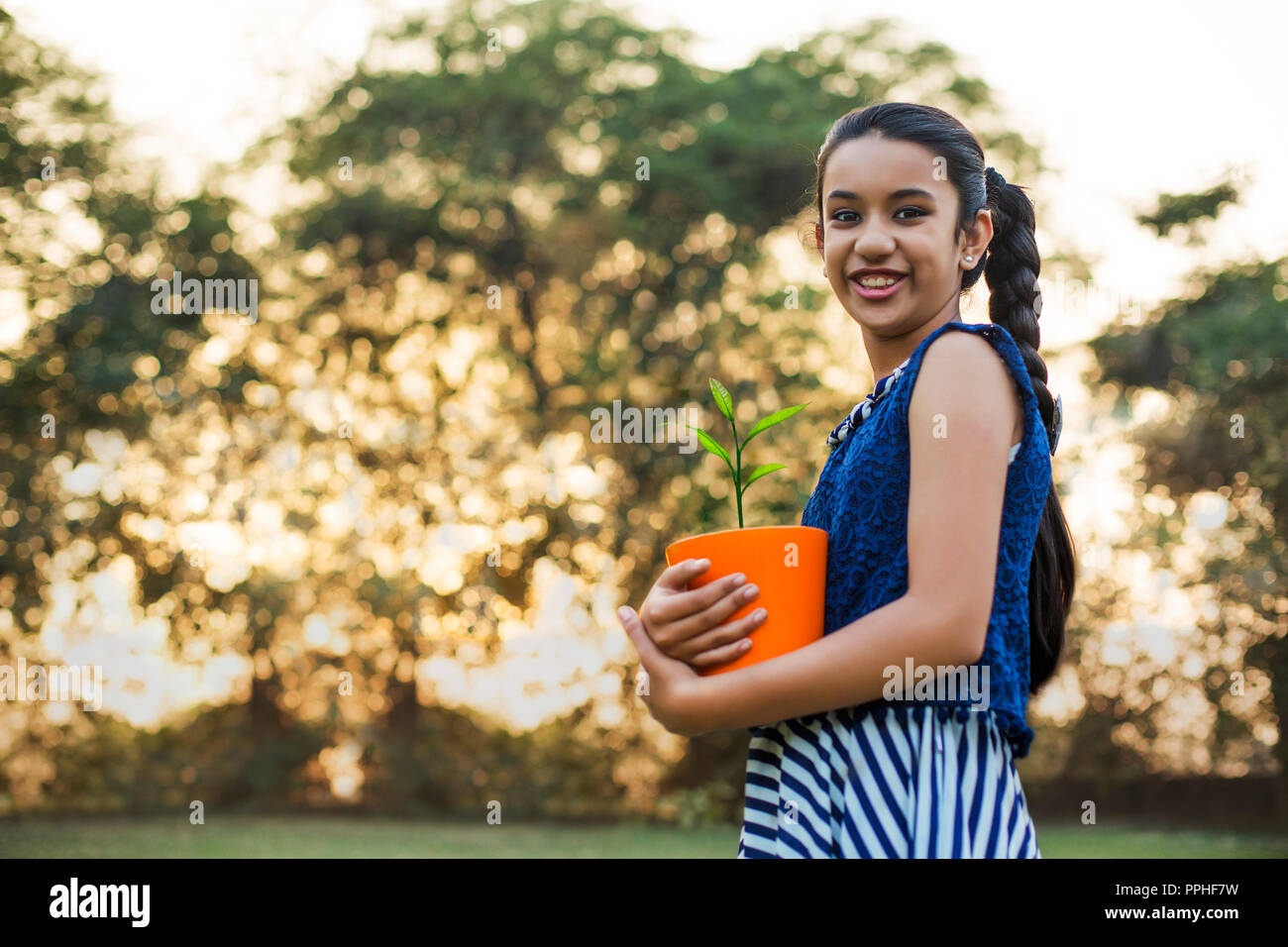 Low Angle View mit einem lächelnden jungen Mädchen mit einem Blumentopf in der Hand im Park. Stockfoto
