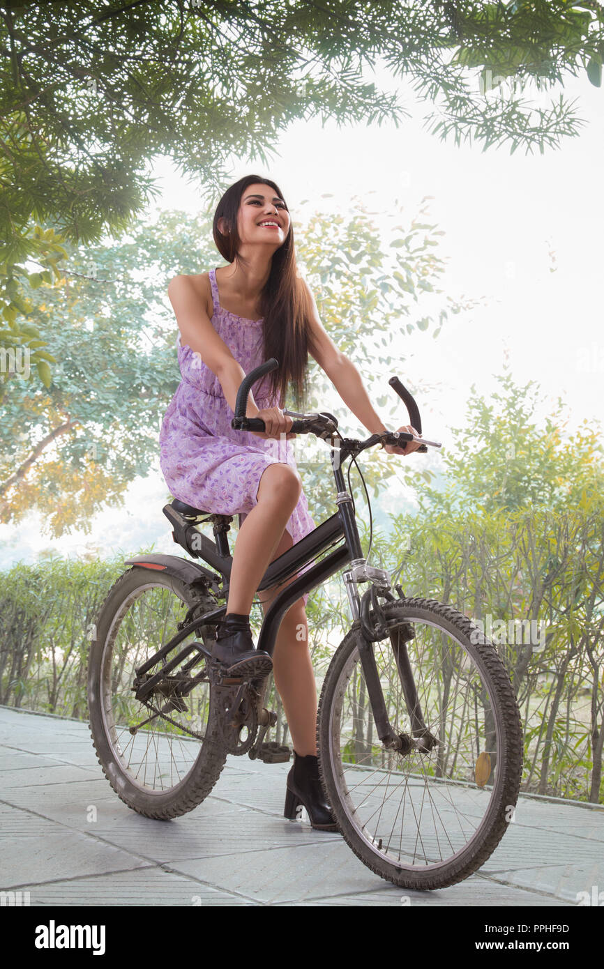 Schöne lächelnde junge Frau sitzt auf einem Fahrrad auf dem Gehweg in einem Park und Spaß haben. Stockfoto