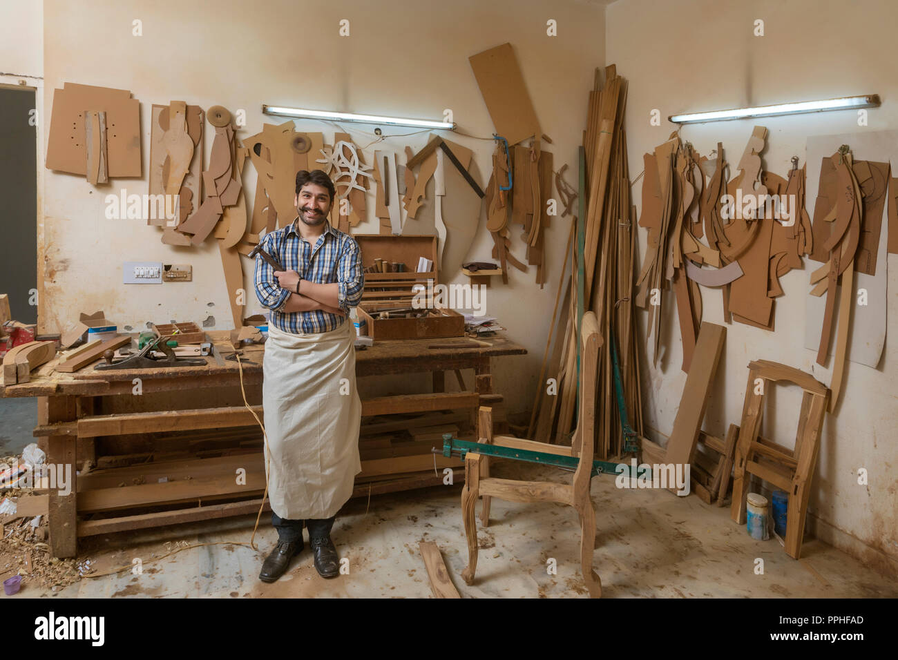 Portrait von Happy Zimmermann in seiner Werkstatt mit einem Hammer mit verschränkten Armen. Stockfoto