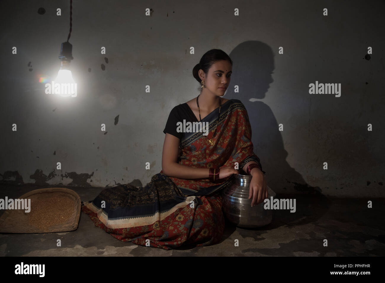 Schönes Dorf, Frau sitzt auf dem Boden mit einer Steel Pot und trennender Ventilator in einem alten schwach beleuchteten Raum und Wegsehen. Stockfoto
