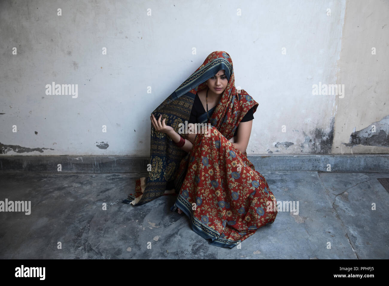 Schöne Frau auf dem Boden sitzend, die ihren Kopf mit Saree blickte nach unten. Stockfoto