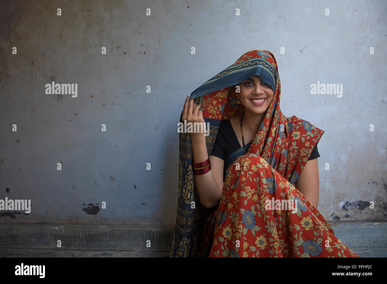 Nahaufnahme von einem schönen Lächeln Frau auf dem Boden sitzend, die ihren Kopf mit Sari. Stockfoto