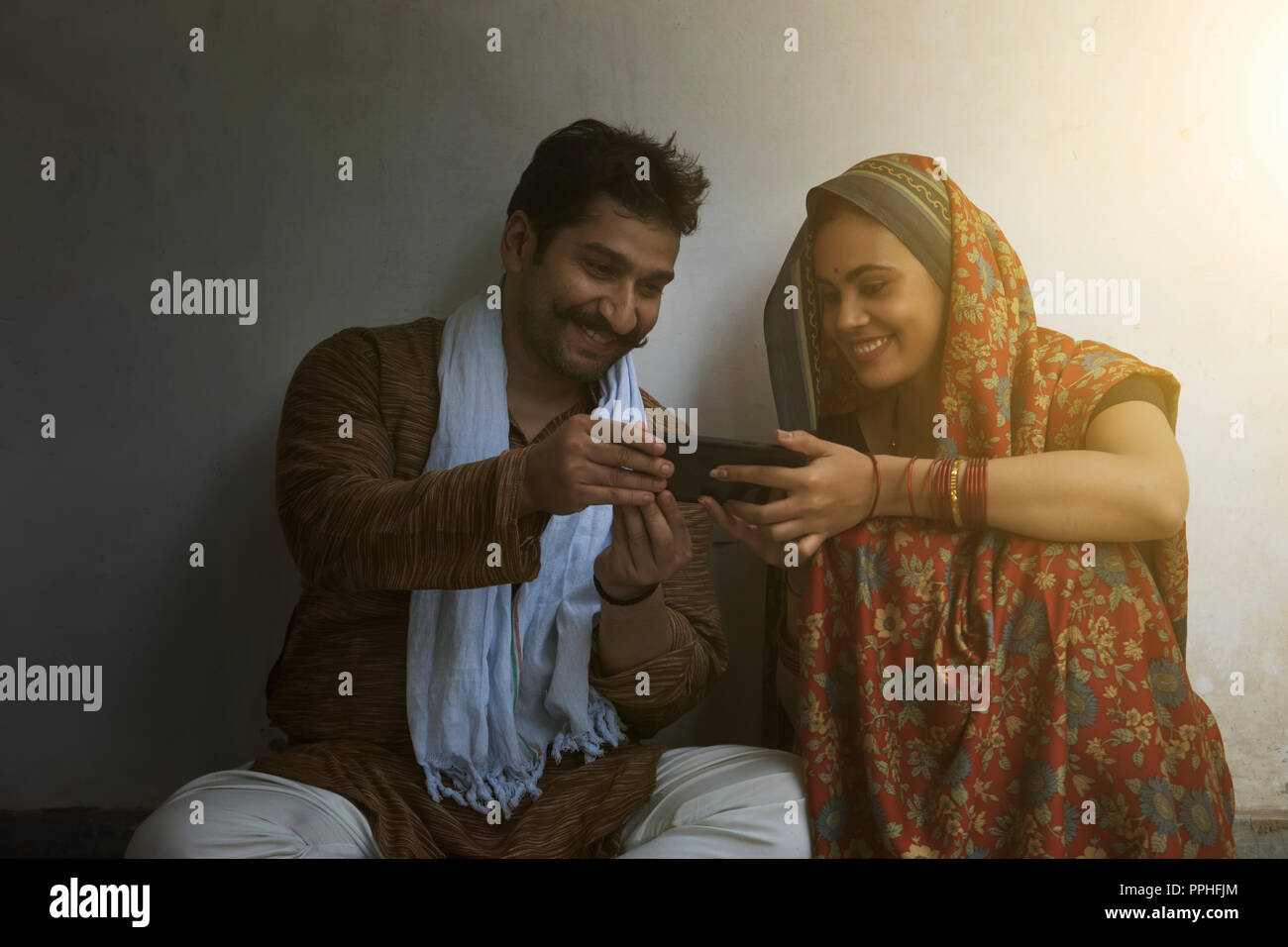 Glücklich und lächelnd ländlichen Paar sitzen auf dem Boden und auf dem Handy. Stockfoto