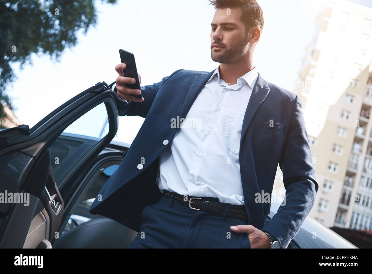 Einen jungen gutaussehenden Mann im Anzug kommt aus dem Auto und nutzt Smartphone Stockfoto