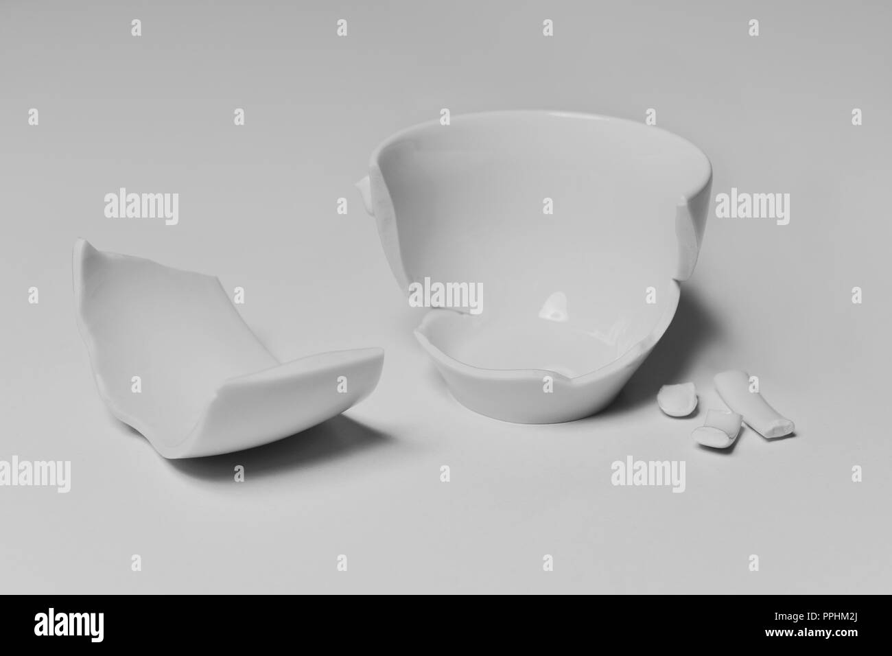 Ein gebrochenes Weiß Keramik Kaffeetasse mit seiner Stücke verteilt auf einem weißen Tisch, vor einem weißen Hintergrund Stockfoto