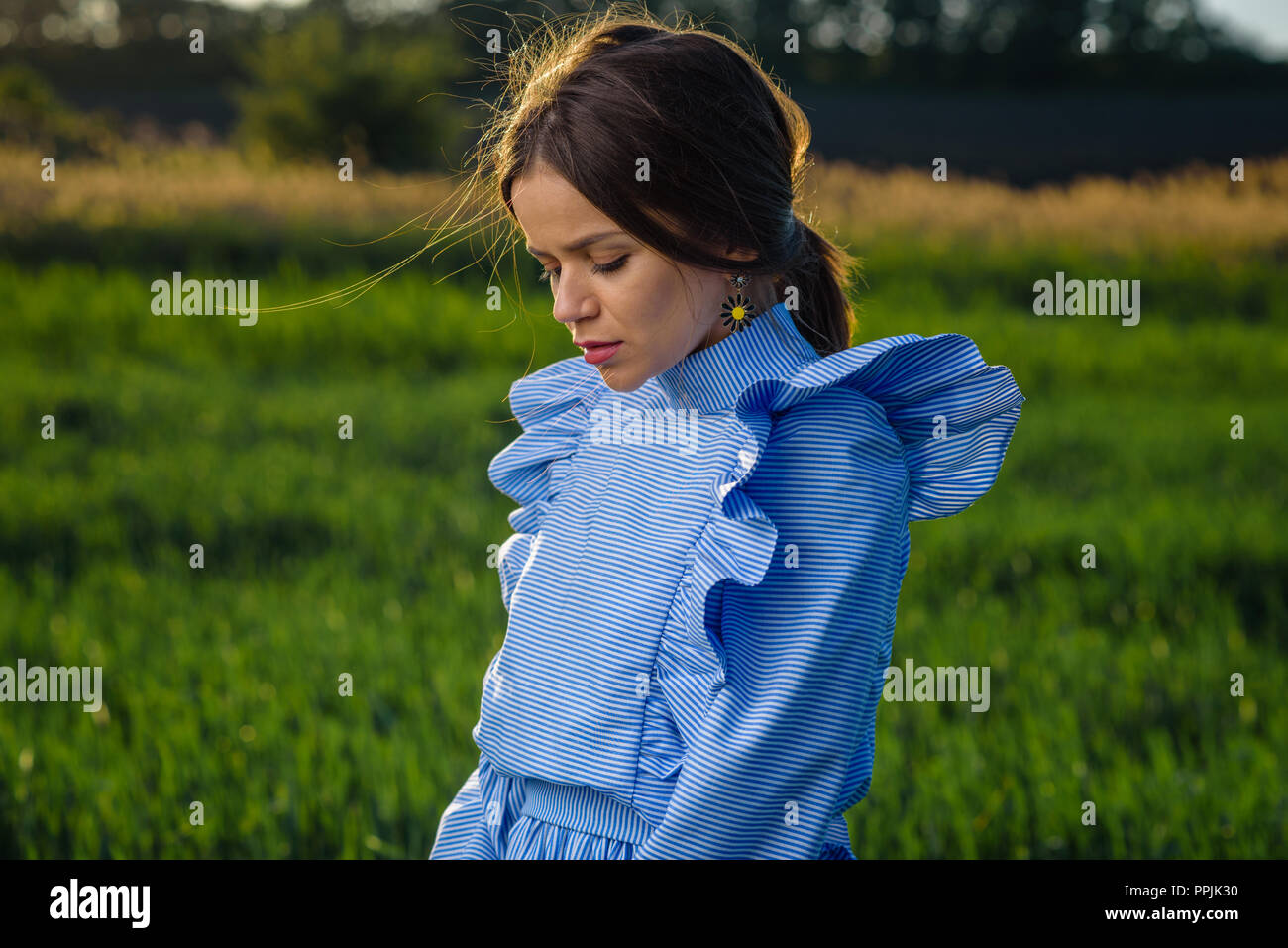 Junge Frau in blau und weiss gestreiftes Kleid ist unten, während im Bereich der grünen Weizen zu einem Frühling Nachmittag stehen bei sonnigem Wetter. Ihr Stockfoto
