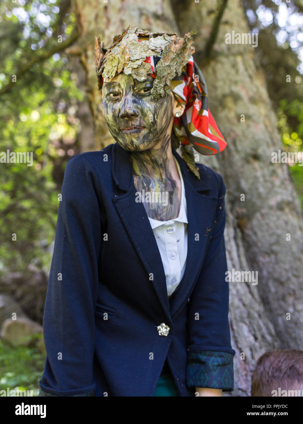 Mädchen Büroangestellter in einen Anzug, im Freien mit einem Make-up im Gesicht imitiert die Rinde eines Baumes. Das Mädchen verschmilzt mit dem Baumstamm, sitzt und Stockfoto