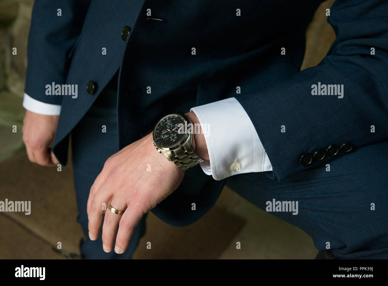 Der junge Mann geeignet Arm mit Shirt Bündchen in seine angehobene Knie gelehnt seinen schwarzen konfrontiert Tissot Uhr und Hochzeit Ring zu zeigen. Stockfoto