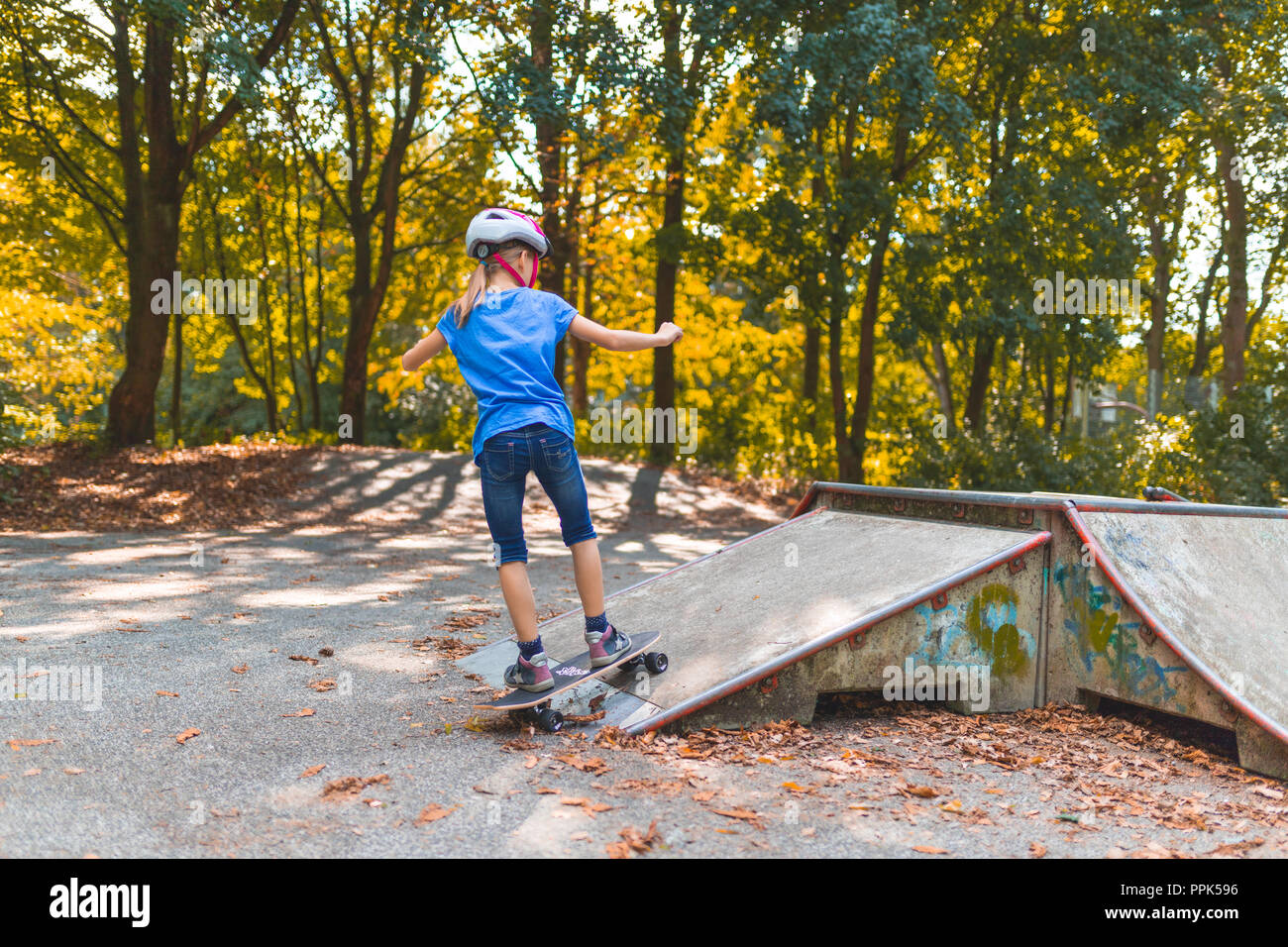 Ein Mädchen Schlittschuhe die Rampe hinauf auf einen Skatepark mit dem Longboard Stockfoto