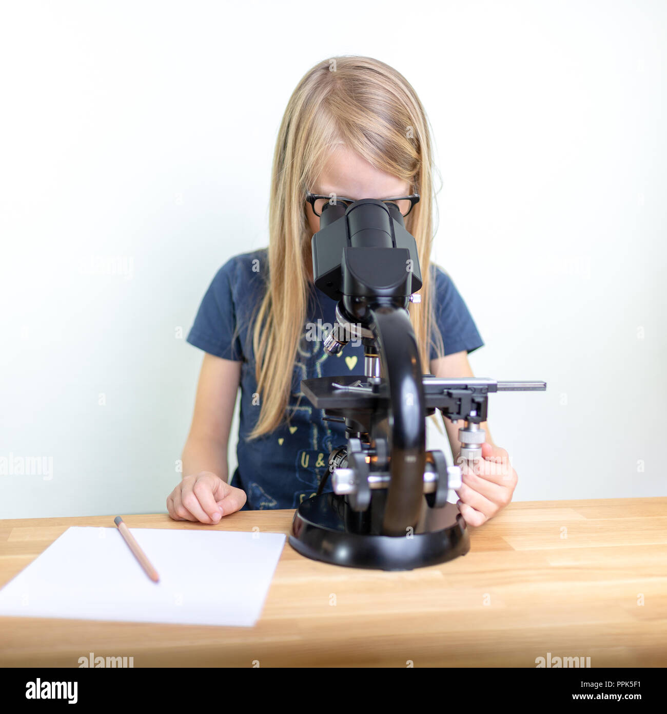 Ein 7-jähriges Mädchen schaut in ein Okular des Mikroskops und Notizen ihre Beobachtungen auf ein Blatt Papier. Vor weißem Hintergrund Stockfoto
