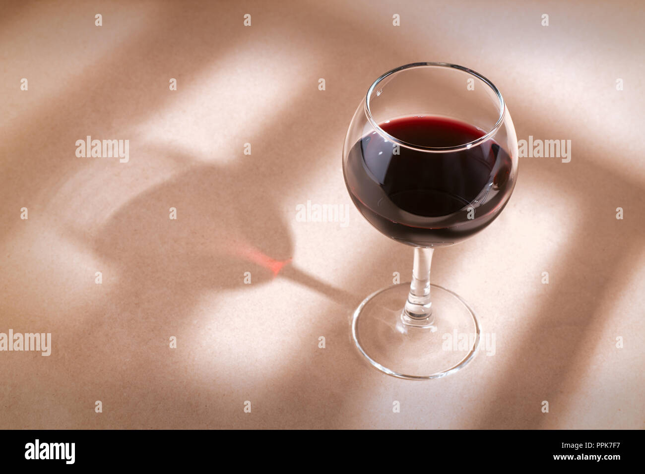 Einzelne rote Wein Glas auf den beige Tabelle mit Fenster Schatten. Stockfoto