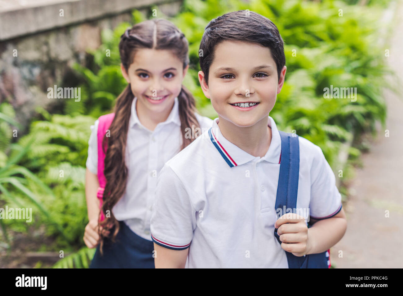 Adorable Schulkinder mit Rucksäcken an Kamera suchen in Park Stockfoto