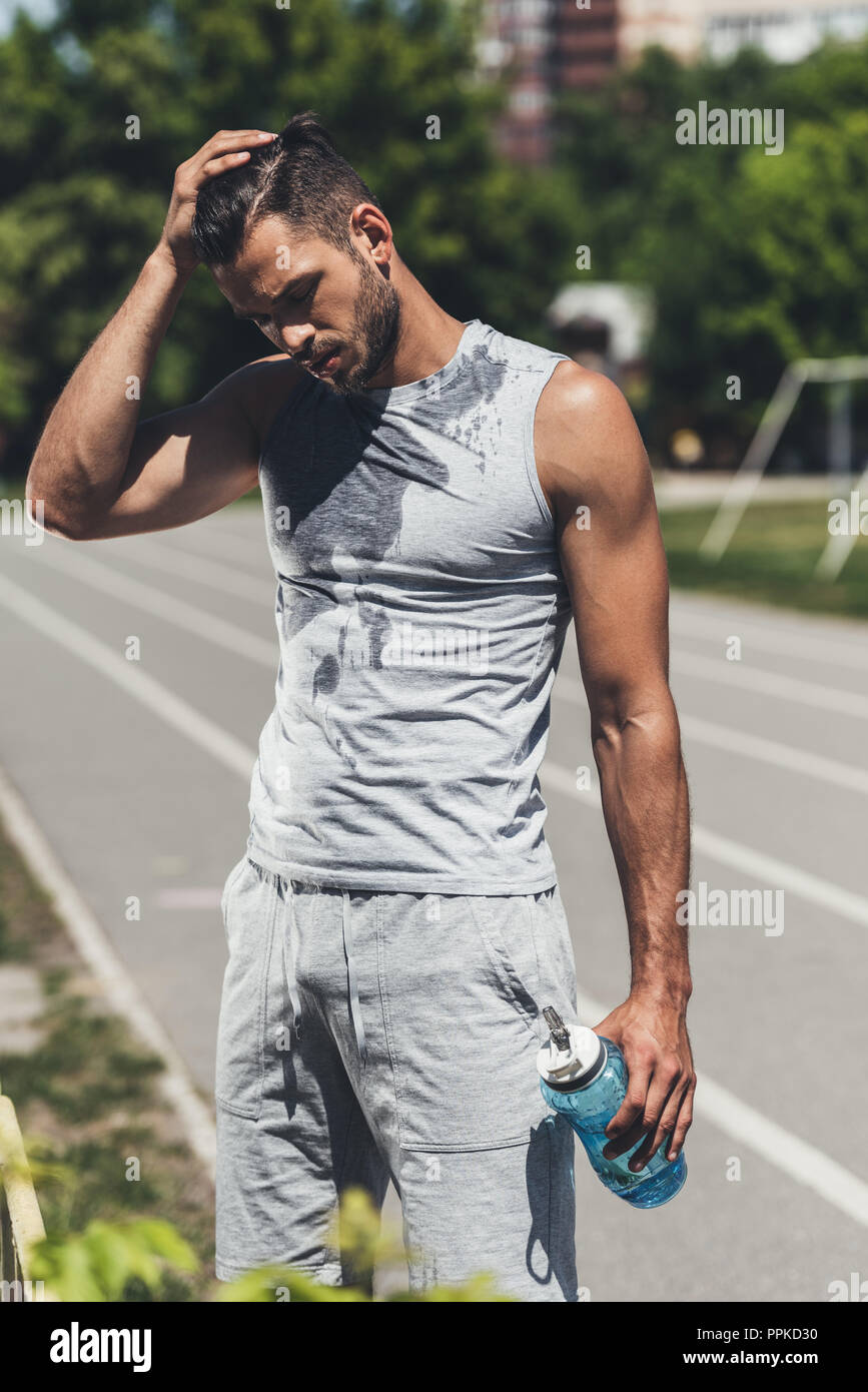 Hübscher junger Mann in wet Shirt mit Fitness Flasche auf Laufbahn Stockfoto