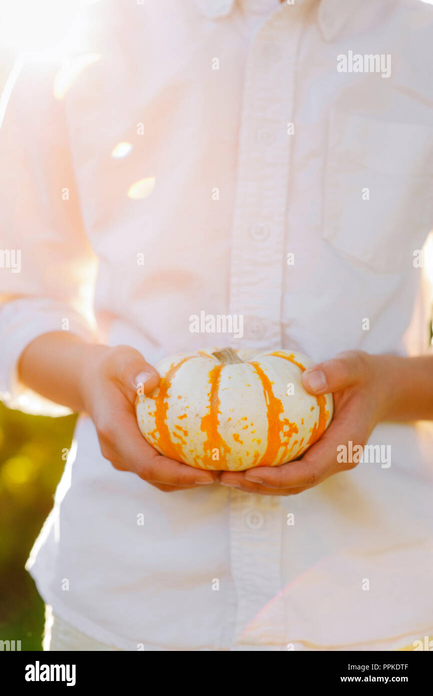 Kleiner Junge mit einem weißen Kürbis mit orangen Streifen Stockfoto