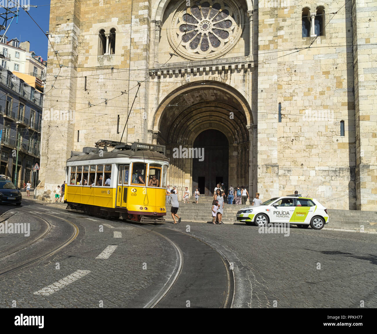Lissabon, Portugal - 31. August 2018: gelbe Tram Linie 28 vor dem Se Kathedrale; Eine nicht identifizierte Junge springt auf eine Straßenbahn. Stockfoto