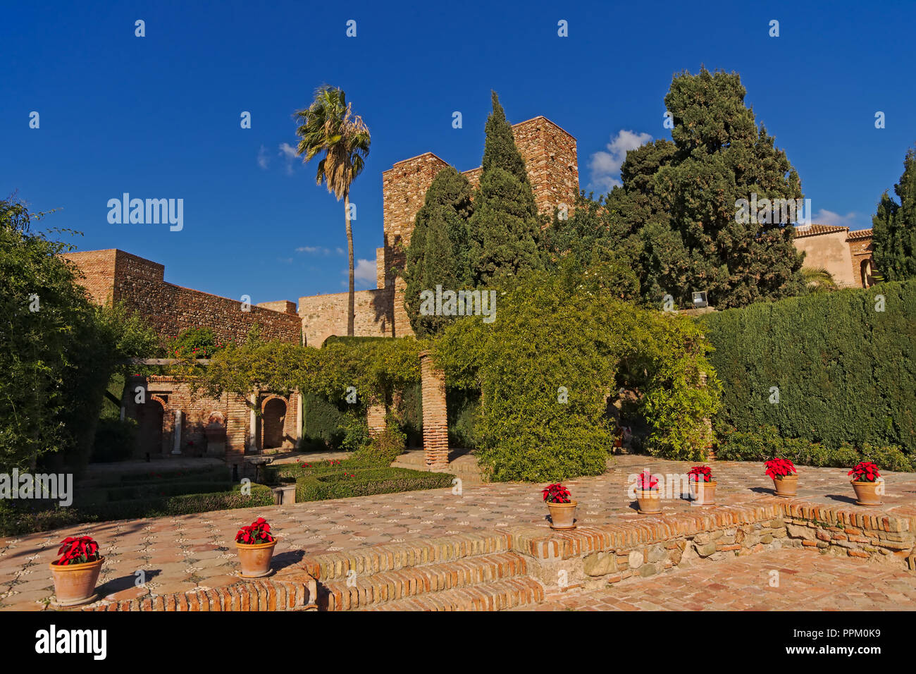 Terrasse mit Blumen und Bäumen der maurischen Burg Alcazaba, Malaga, von grünen Pflanzen umgeben an einem sonnigen Tag mit blauen Himmel Stockfoto