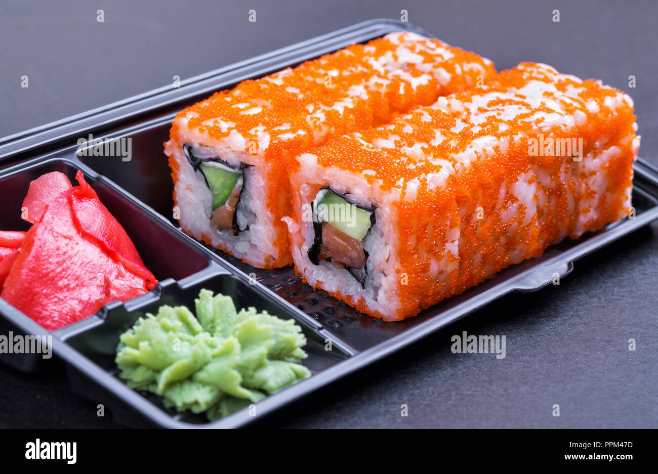 Satz von California Rolls in einem schwarzen 'take away'-Container auf einem schwarzen Hintergrund Seitenansicht Stockfoto