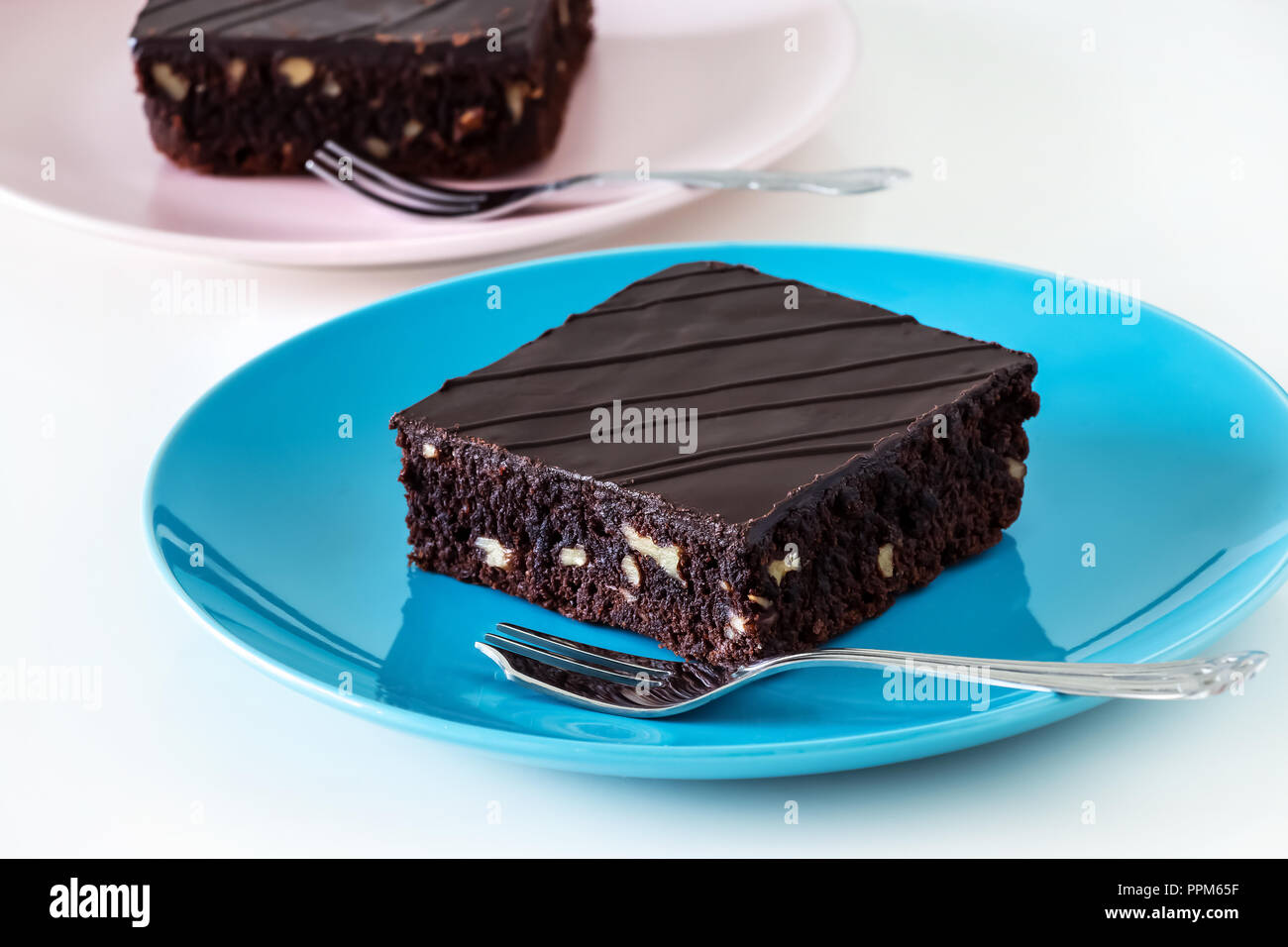 Dunkle Schokolade veganer Schokoladenkuchen Kuchen mit Muttern blau und rosa Platte weißen Hintergrund. Selektive konzentrieren. Stockfoto