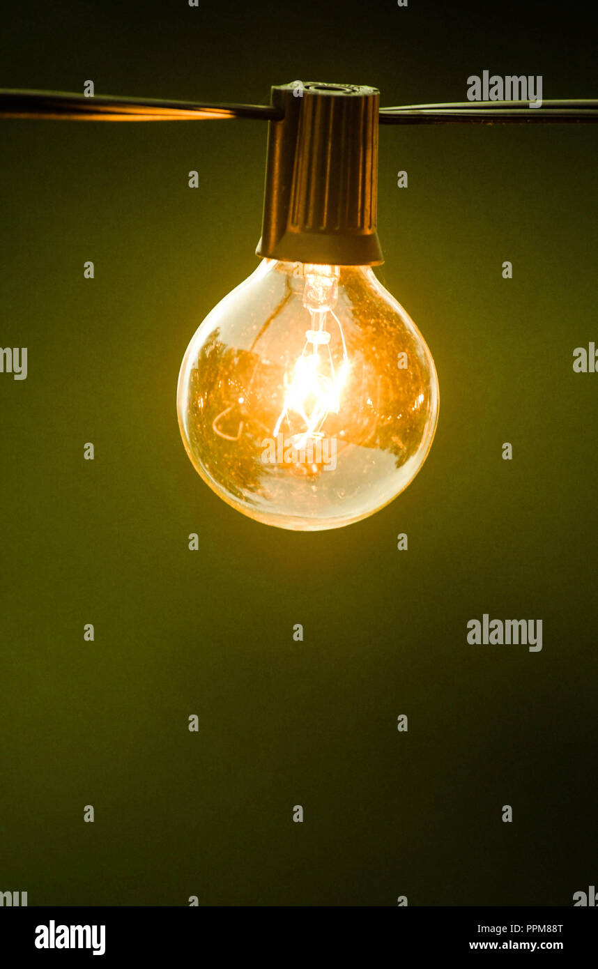 Eine Glühbirne, leuchtende Gelb, hängend an einem schwarzen Kabel in den frühen Abend. Stockfoto