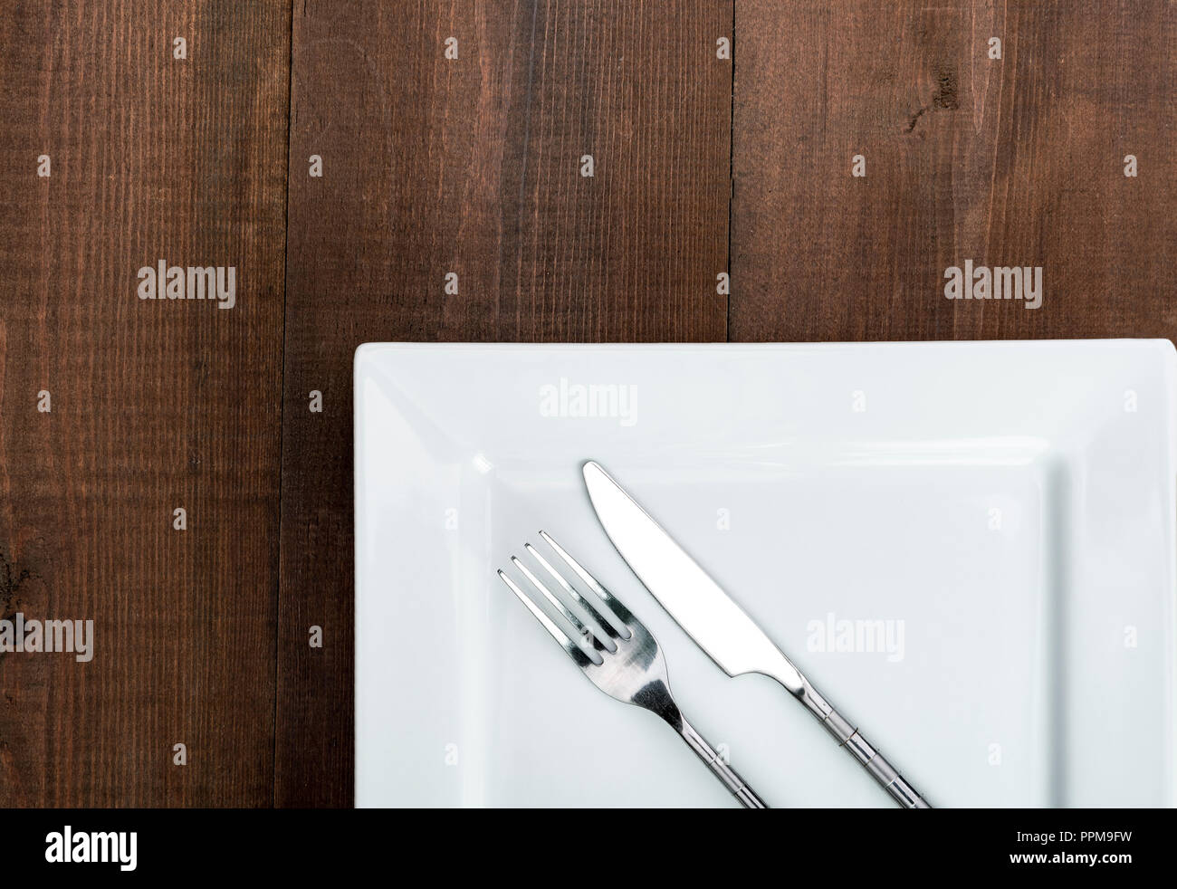 Quadratische weiße Teller auf einen hölzernen Tisch mit Messer und Gabel. Stockfoto