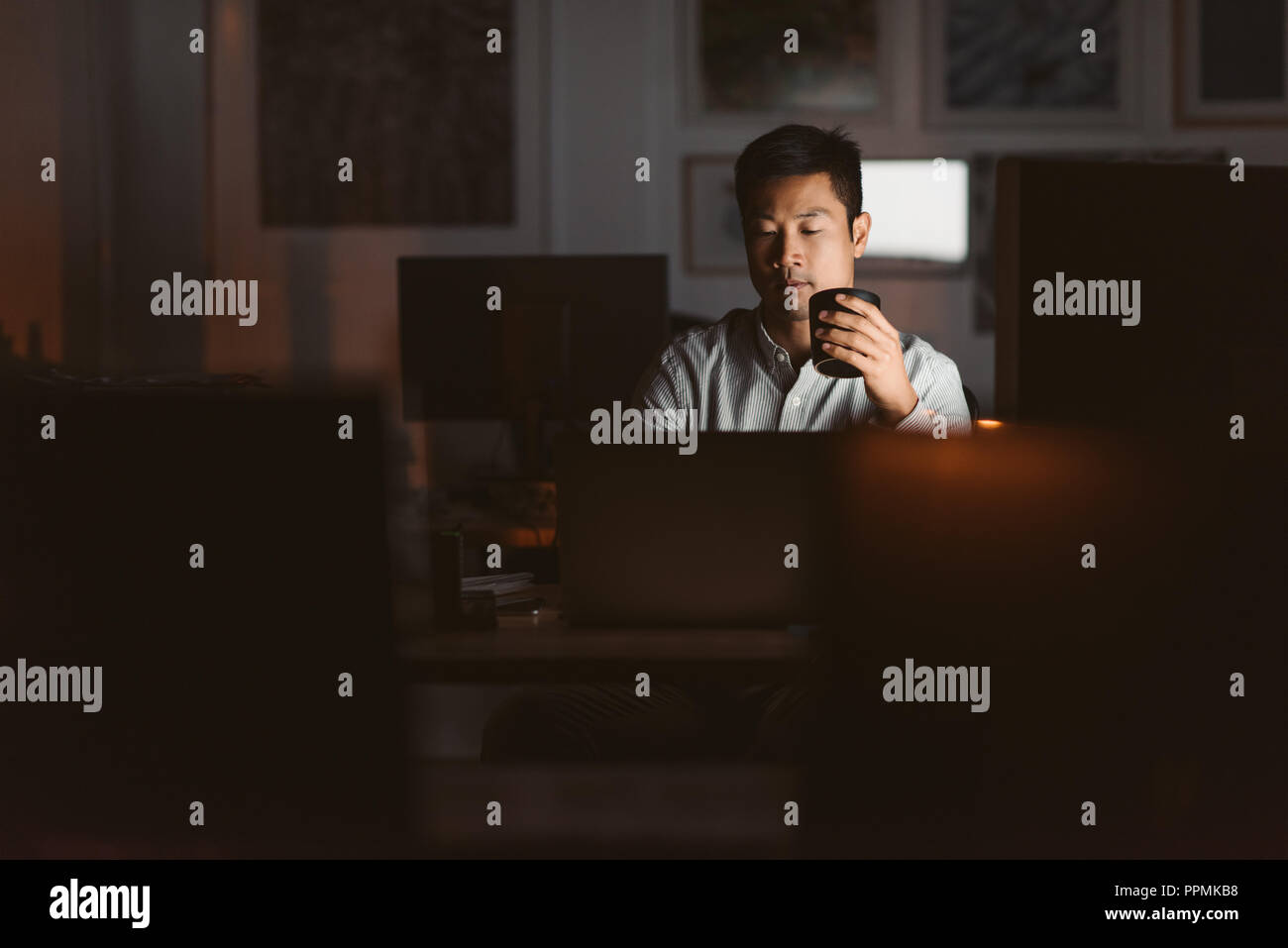 Junge asiatische Geschäftsmann an seinem Schreibtisch die Arbeit in einem Büro spät in der Nacht Trinken einer Tasse Kaffee, um wach zu bleiben Stockfoto