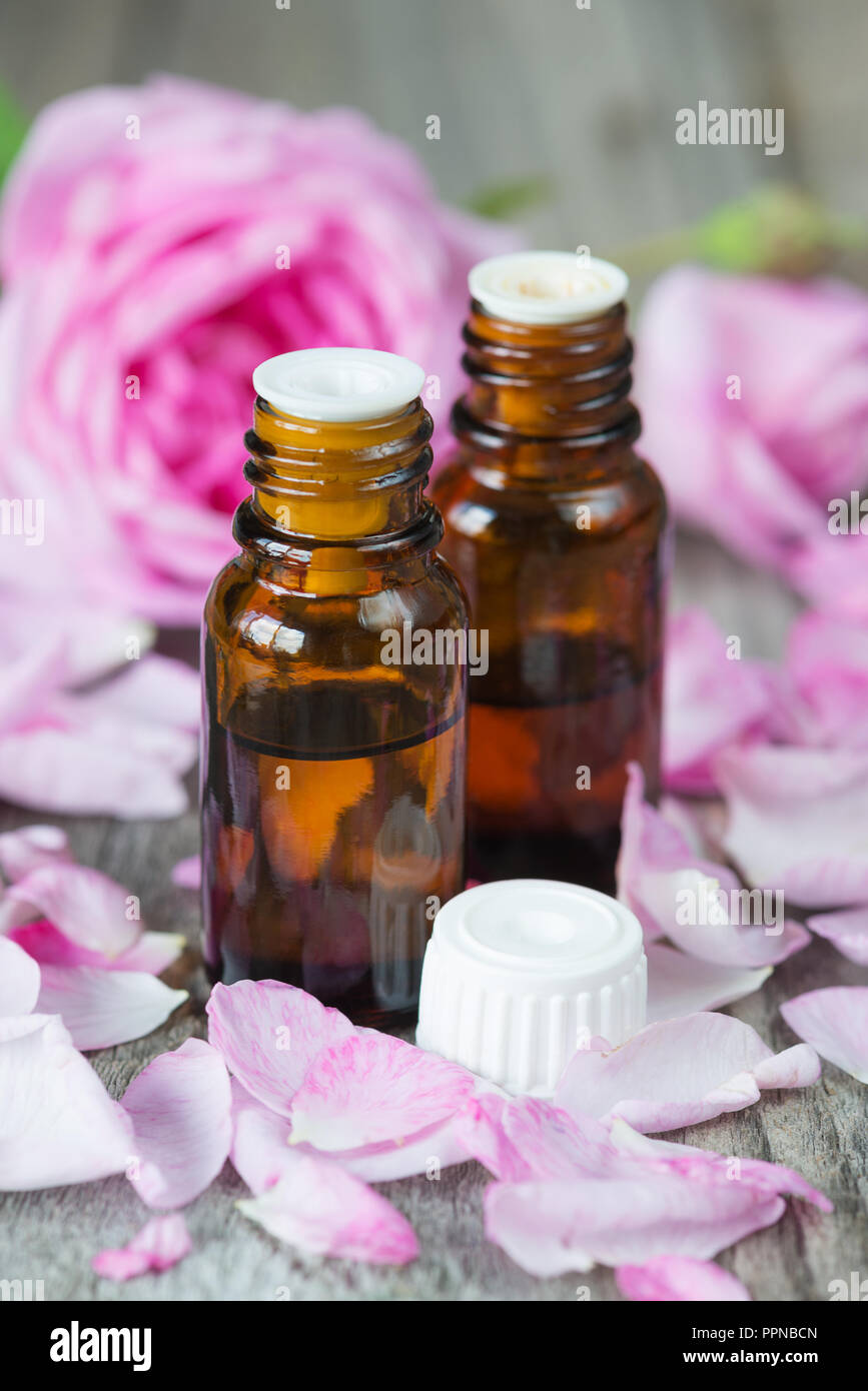 Zwei dunkle Durchstechflaschen mit Rose ätherisches Öl und Rosen auf einem hölzernen Hintergrund Stockfoto