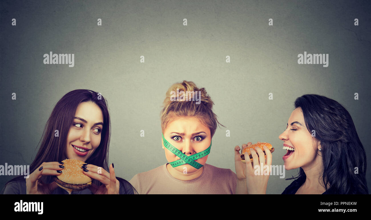 Mollige Frau mit Mund mit Maßband mit glücklichen Frauen essen Burger umgeben ist abgeschaltet Stockfoto