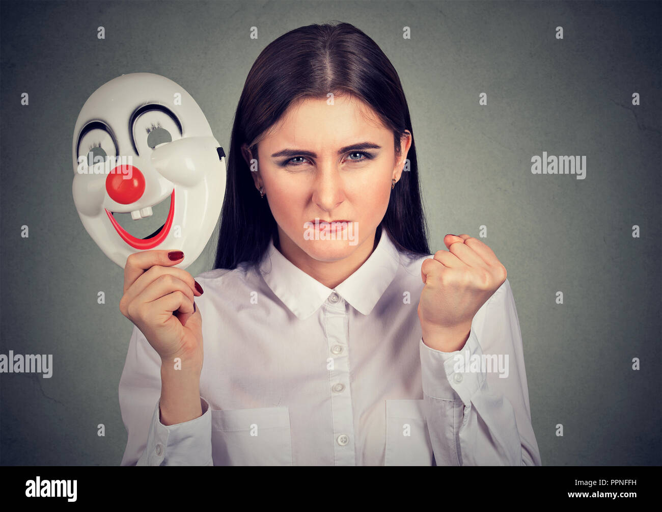 Junge Frau mit gespaltene Persönlichkeit suchen super an Kamera wütend, während clown Maske zu verbergen Stockfoto