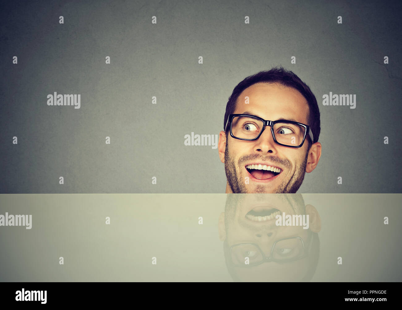 Nach verrückten Mann in Gläsern peeking unter dem Tisch und weg schauen auf grauem Hintergrund Stockfoto