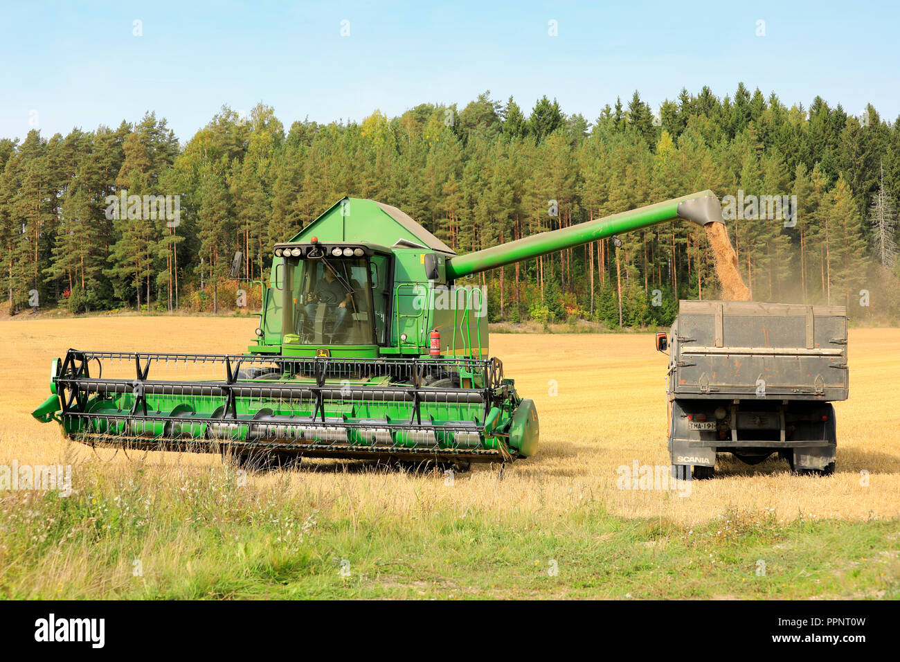 Salo, Finnland - 8 September, 2018: John Deere Mähdrescher entlädt geernteten Getreide auf LKW-Anhänger an einem klaren Tag der Herbst im Süden Finnlands. Stockfoto