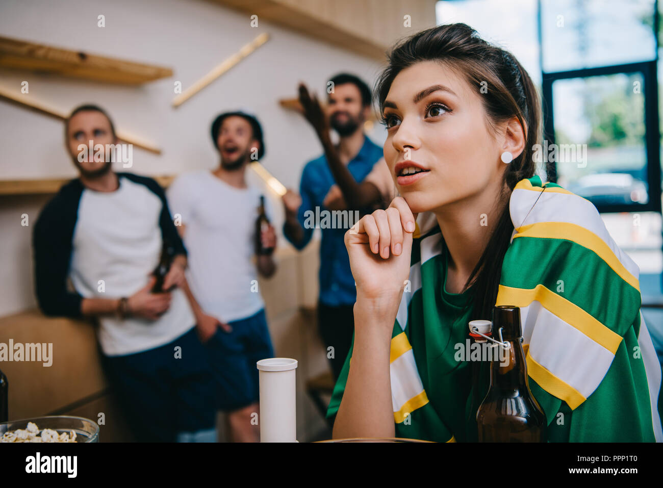 Frau in Grün Lüfter t-shirt und Fan-schal und Ihre männlichen Freunde hinter stehen während der Nachtwache Fußballspiel an der Bar Stockfoto