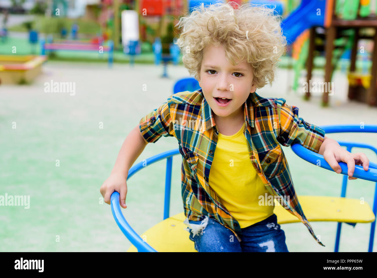 Selektiver Fokus von Curly kleiner Junge reiten auf Karussell am Spielplatz Stockfoto