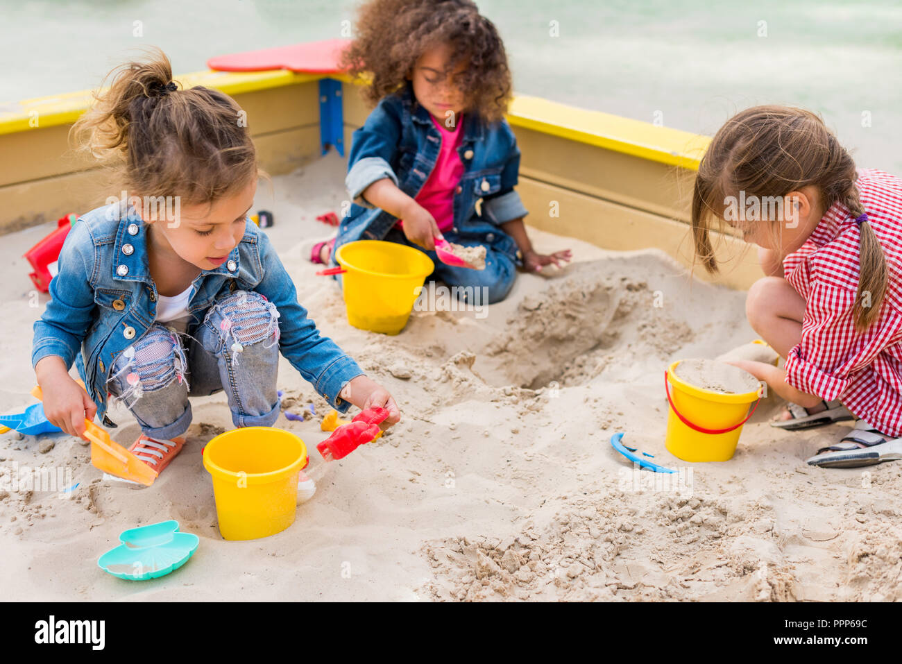 Drei multiethnischen kleine Kinder spielen mit Kunststoff schaufeln und Eimer in Sandbox am Spielplatz Stockfoto