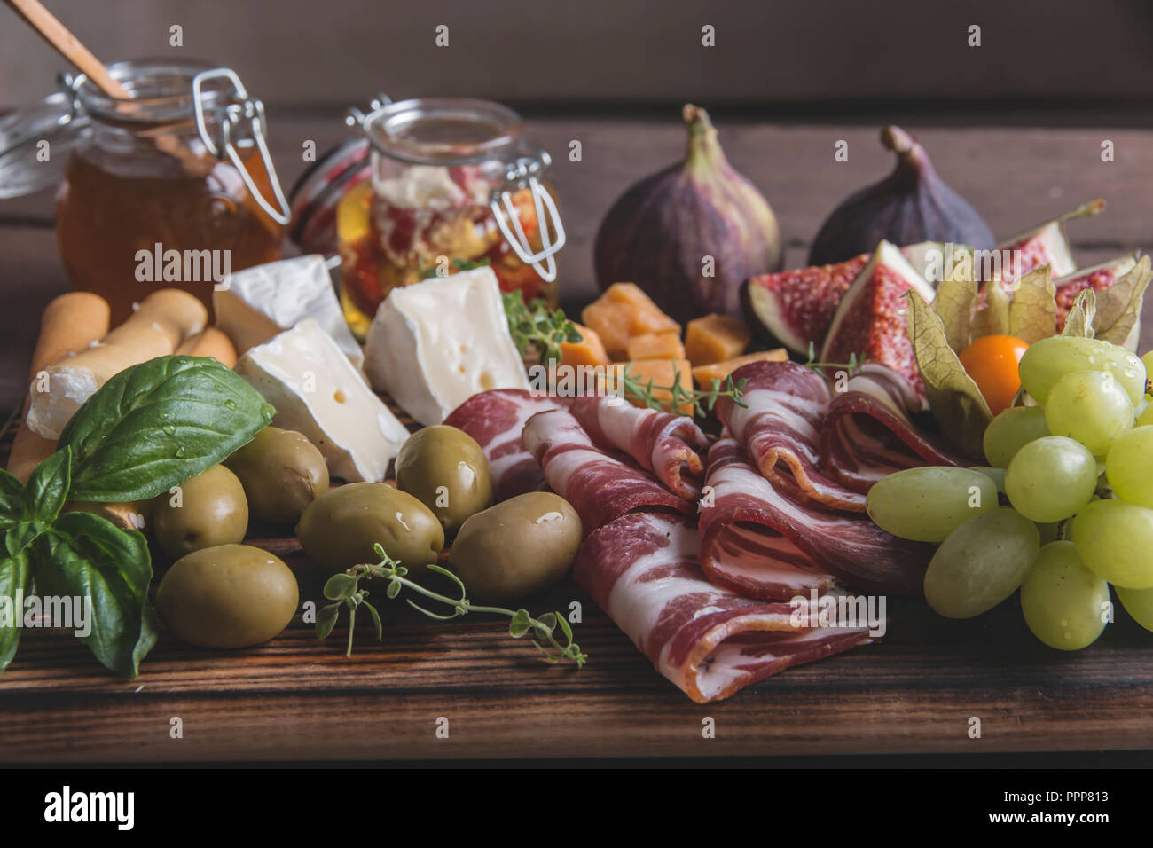 Prosciutto, Camembert, Feigen, Honig, Trauben, Oliven auf dunklen, das Brett über rustikal Hintergrund Stockfoto
