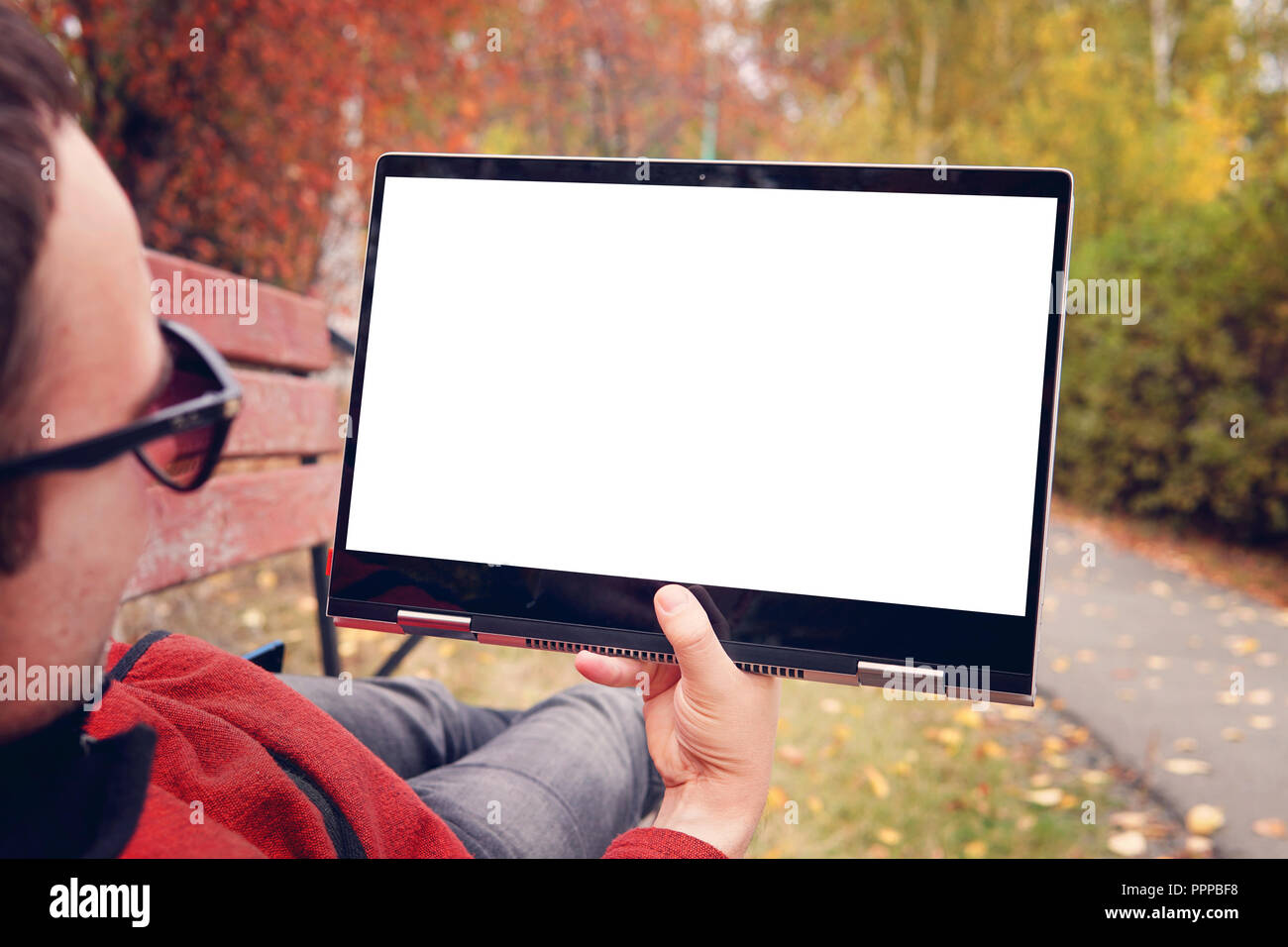 Mann liegt auf einer Bank im Herbst Park und schaut auf den Bildschirm eines modernen ultrabook Transformator. Blank Screen für Design. Erholung im Freien. Stockfoto